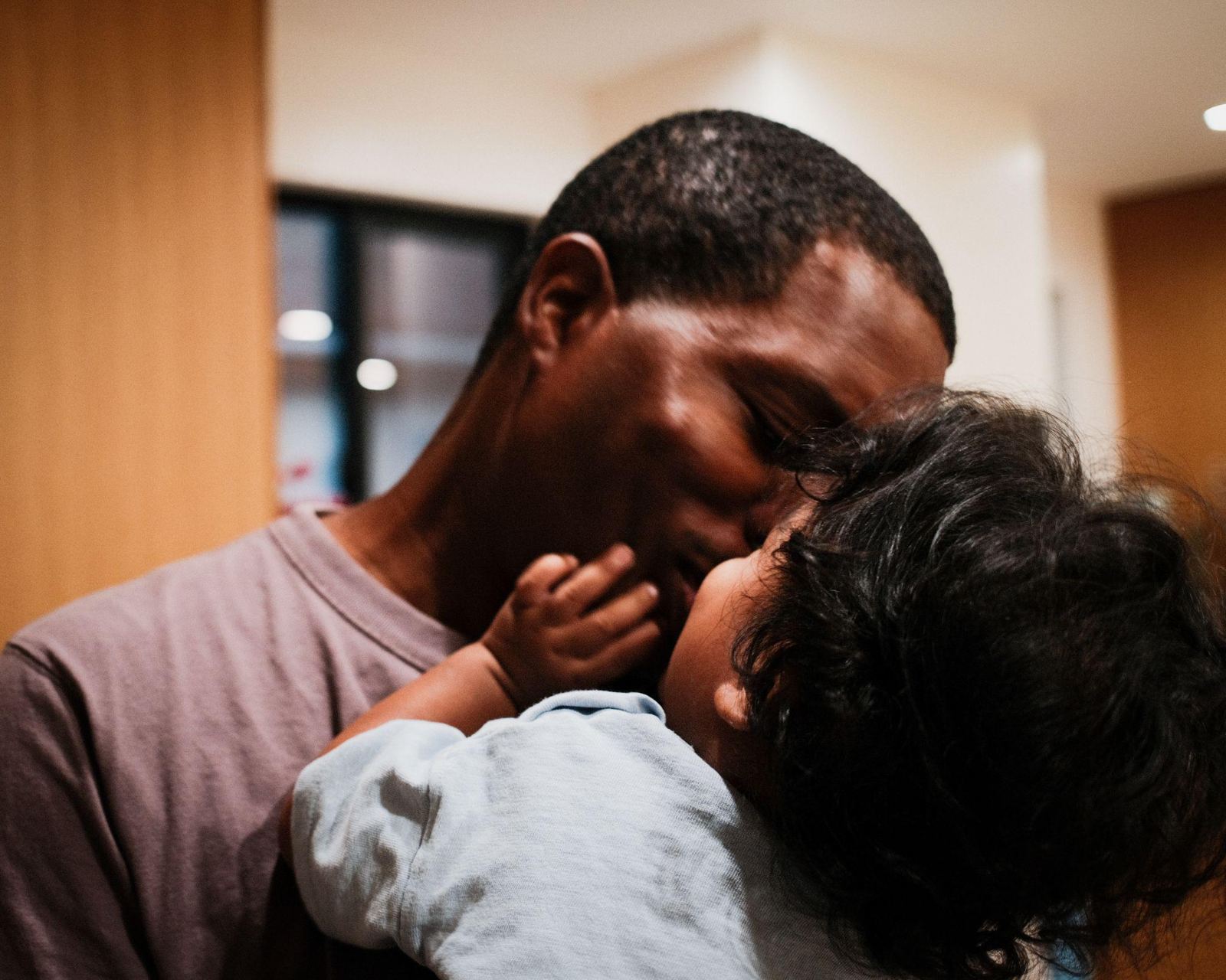 A father kisses his toddler son, who holds his father's face with one hand.